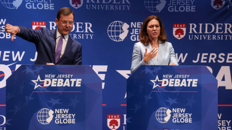 Two candidates at blue debate podiums; a man gives a thumbs-down while a woman speaks with her hand on her chest.